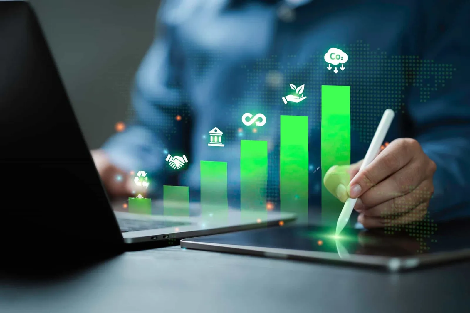 Person with a stylus and tablet beside a laptop, with a glowing green bar chart and sustainability icons rising above.